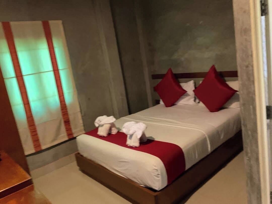 A hotel room with a bed, pillows, and a red blanket.
