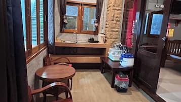 A compact kitchen with a dining area, a window with curtains, a fan, and a small table with chairs.