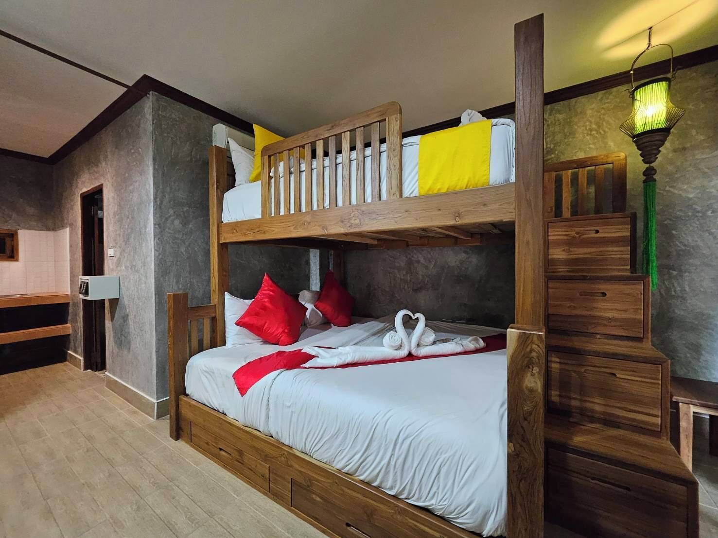 Een stapelbed met witte beddengoed en rode kussens, een houten bankje en een trap.