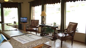 A hotel lobby with a reception desk, two leather armchairs, a television, a lamp, and a potted plant. - Green Gables Inn (Branson)