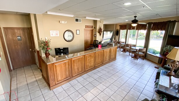 A reception area with a wooden counter, a clock, and a sign indicating a 6:10 meeting time. - Green Gables Inn (Branson)
