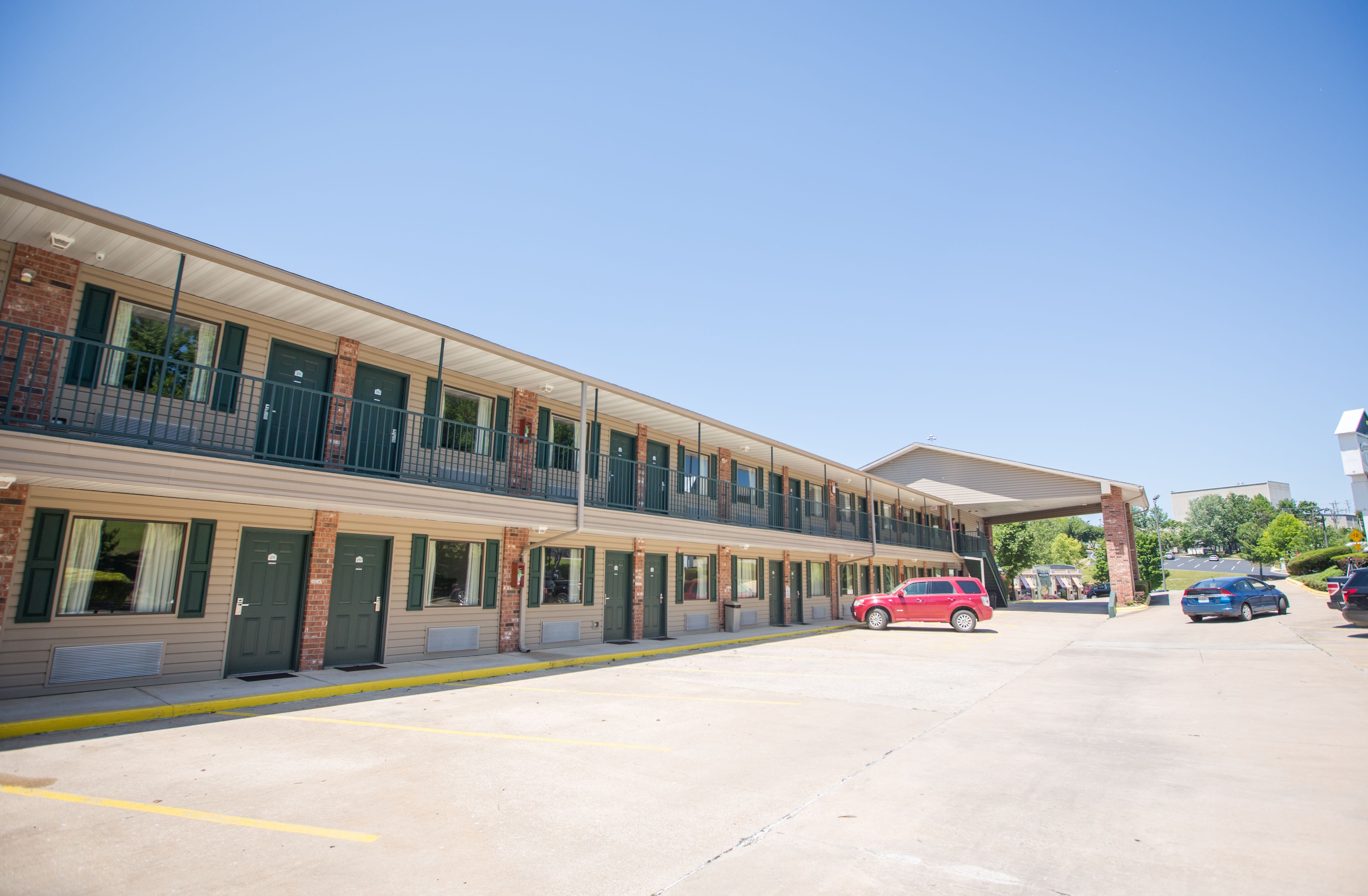 A motel with a two-story structure, a covered parking area, and a row of rooms with green doors.