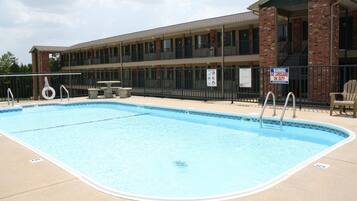 A swimming pool with a lifeguard stand, a covered seating area, and a building with a brick facade.