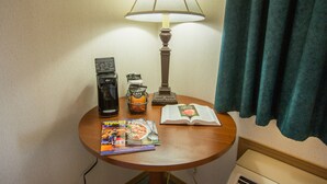 A small wooden table with a lamp, a coffee maker, a jar of coffee creamer, a book, and a travel magazine. - Green Gables Inn (Branson)