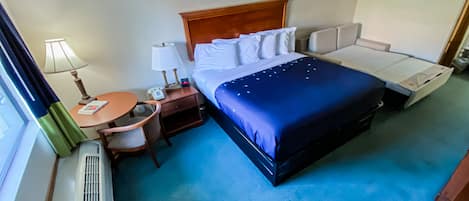 A hotel room with a large bed, a bedside table with a lamp, a small round table, and a chair.