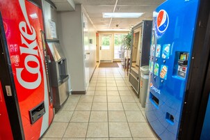 A hallway with vending machines for Coke and Pepsi, a trash bin, and a door leading to a room.