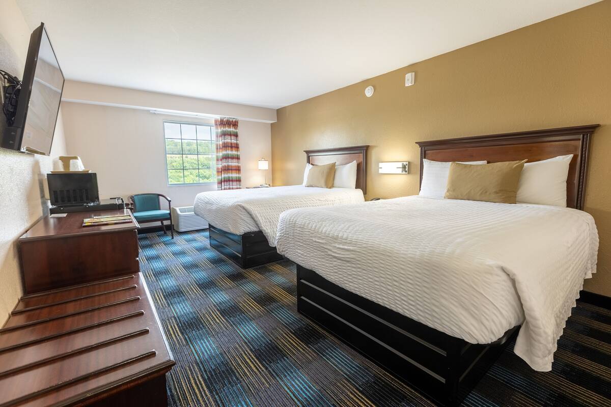 A hotel room with two beds, a desk, a chair, and a large window.