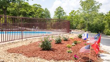 A landscaped area with a pool, surrounded by a metal fence, and adorned with American flags and flowers.