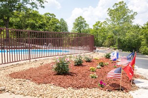 A landscaped area with a pool, surrounded by a metal fence, and adorned with American flags and flowers.