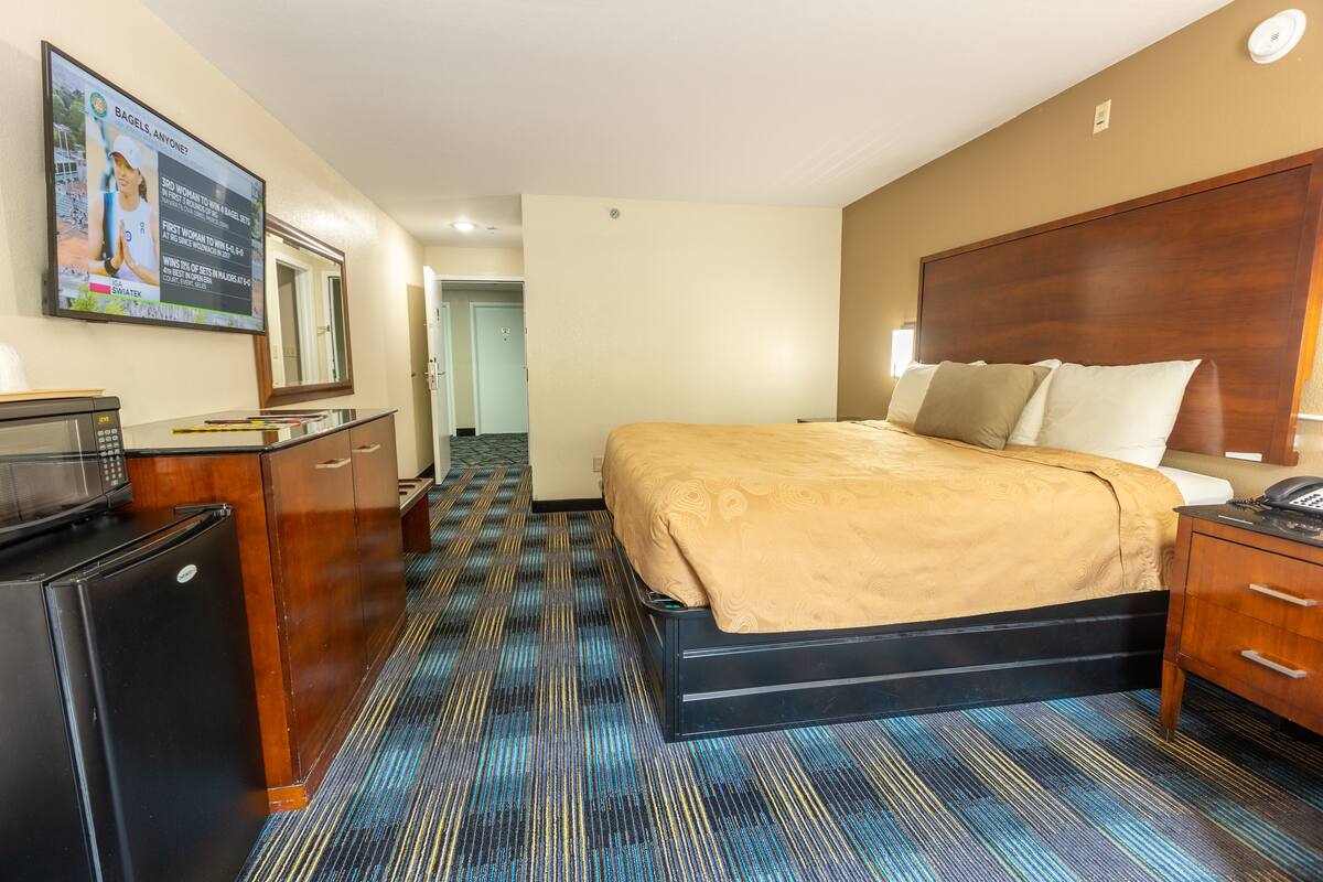 A hotel room with a bed, a desk with a computer, a microwave, and a large mirror on the wall.