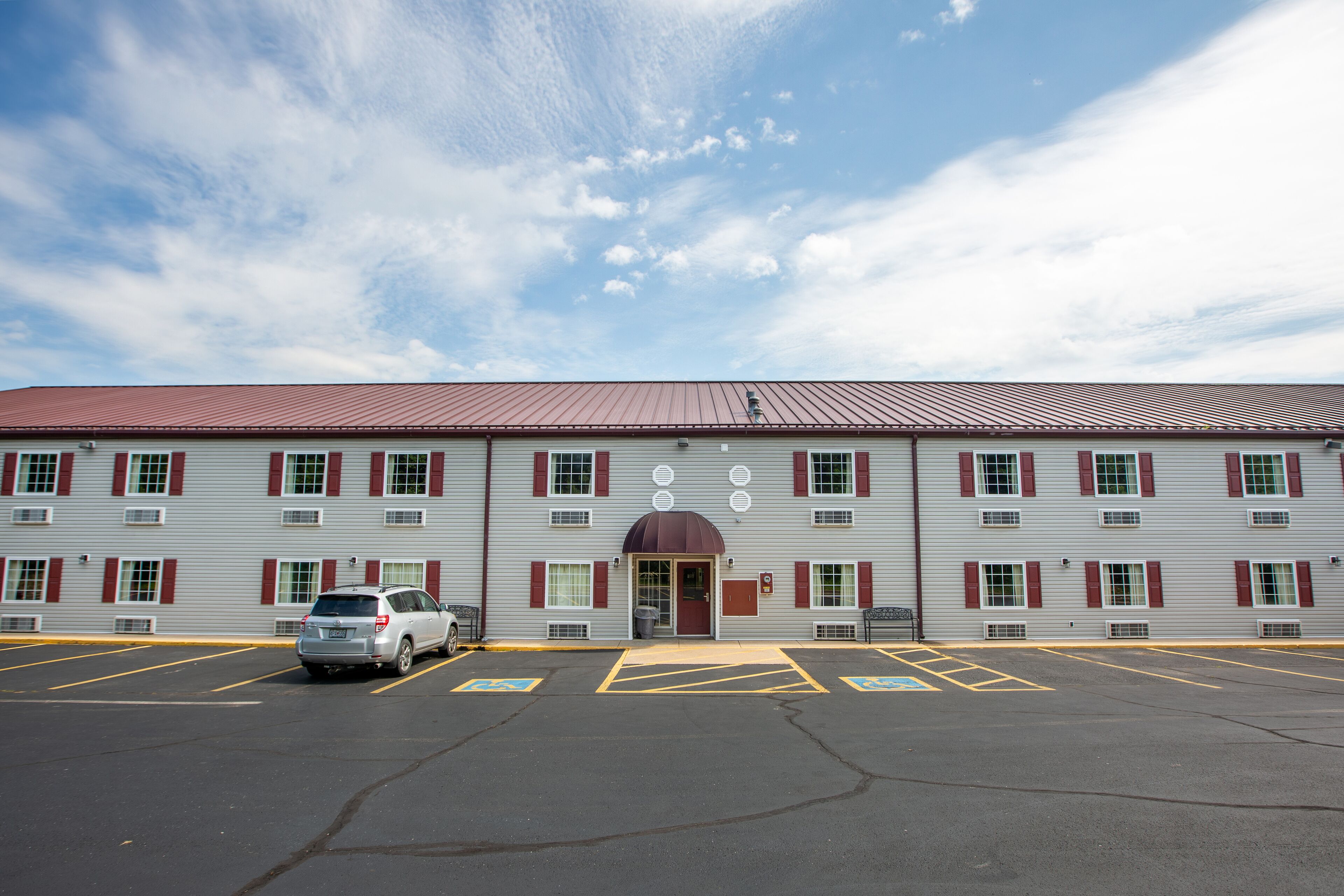 A building with a red roof and multiple windows with red shutters. There is a parking lot in front with marked handicapped spaces.