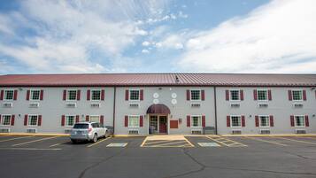 A building with a red roof and multiple windows with red shutters. There is a parking lot in front with marked handicapped spaces.