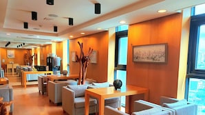 A modern hotel lobby with wooden paneling, comfortable seating, a coffee machine, and a view of the city through large windows. - Hotel Rian (Seoul)