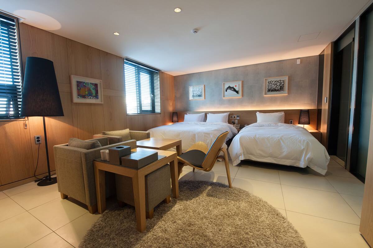 A modern hotel room with a sofa, two beds, a table, and artwork on the walls.