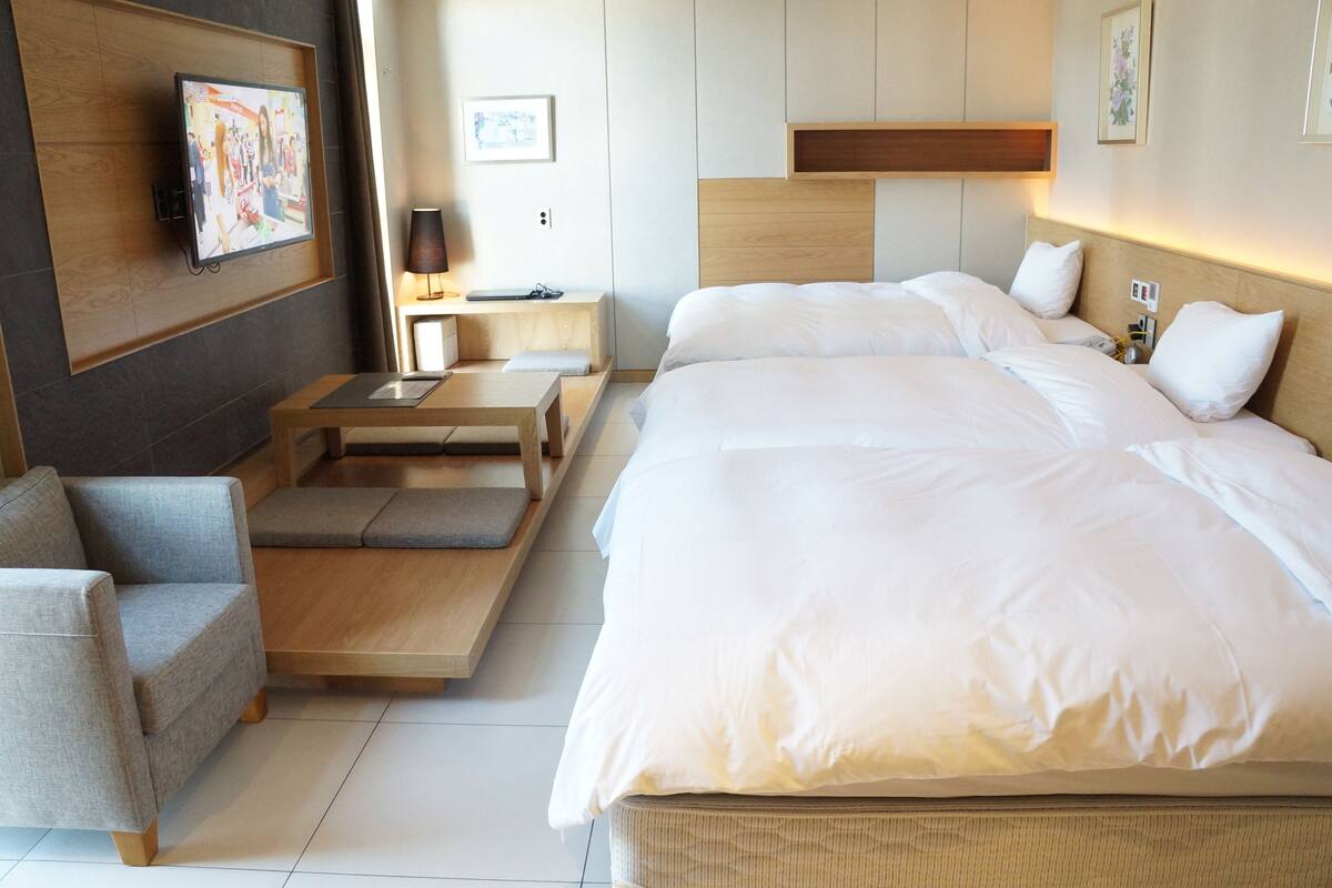 A hotel room with a large bed, a sofa, a desk, and a TV on the wall.