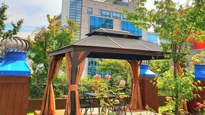 A gazebo with a wooden structure and metal roof, surrounded by greenery and a modern building in the background. - Hotel Rian (Seoul)