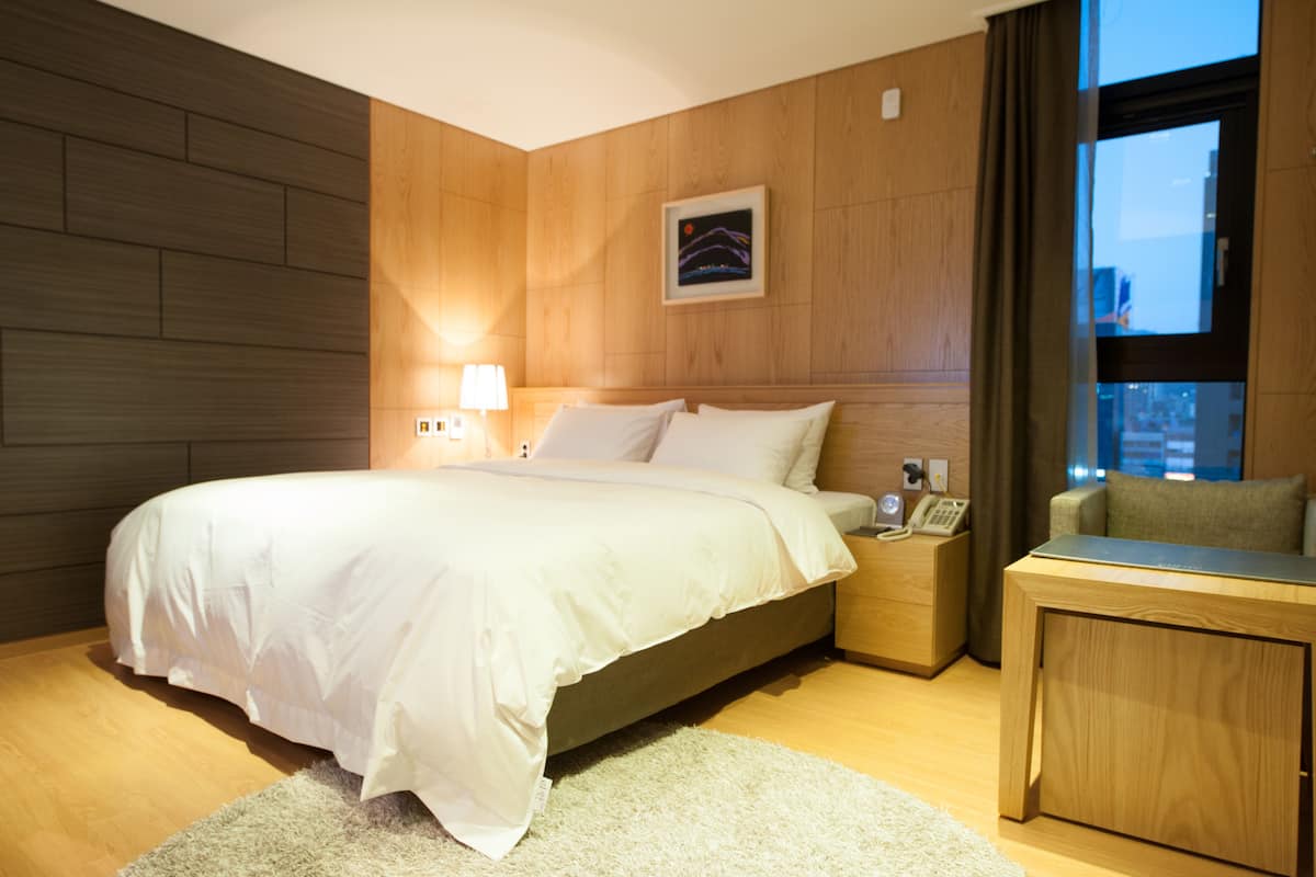A modern hotel room with a large bed, bedside table, and a small seating area.