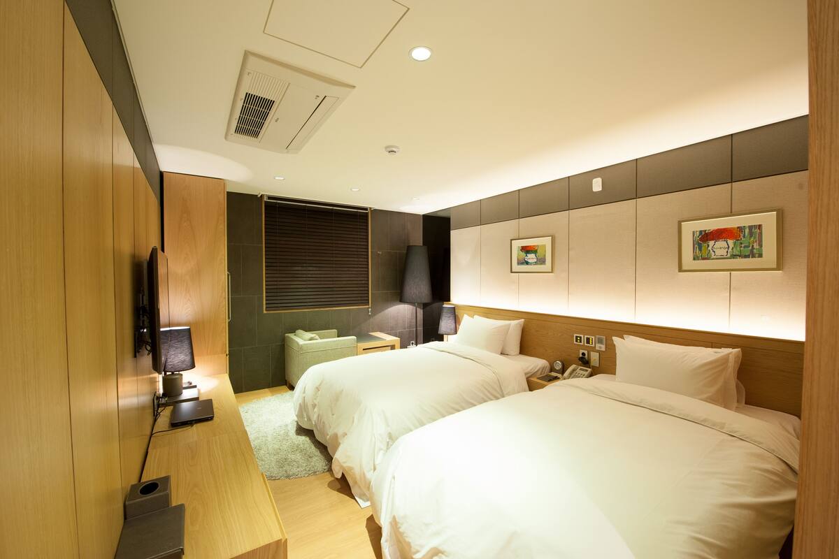 A hotel room with two beds, a desk with a computer, a TV, and a small seating area.