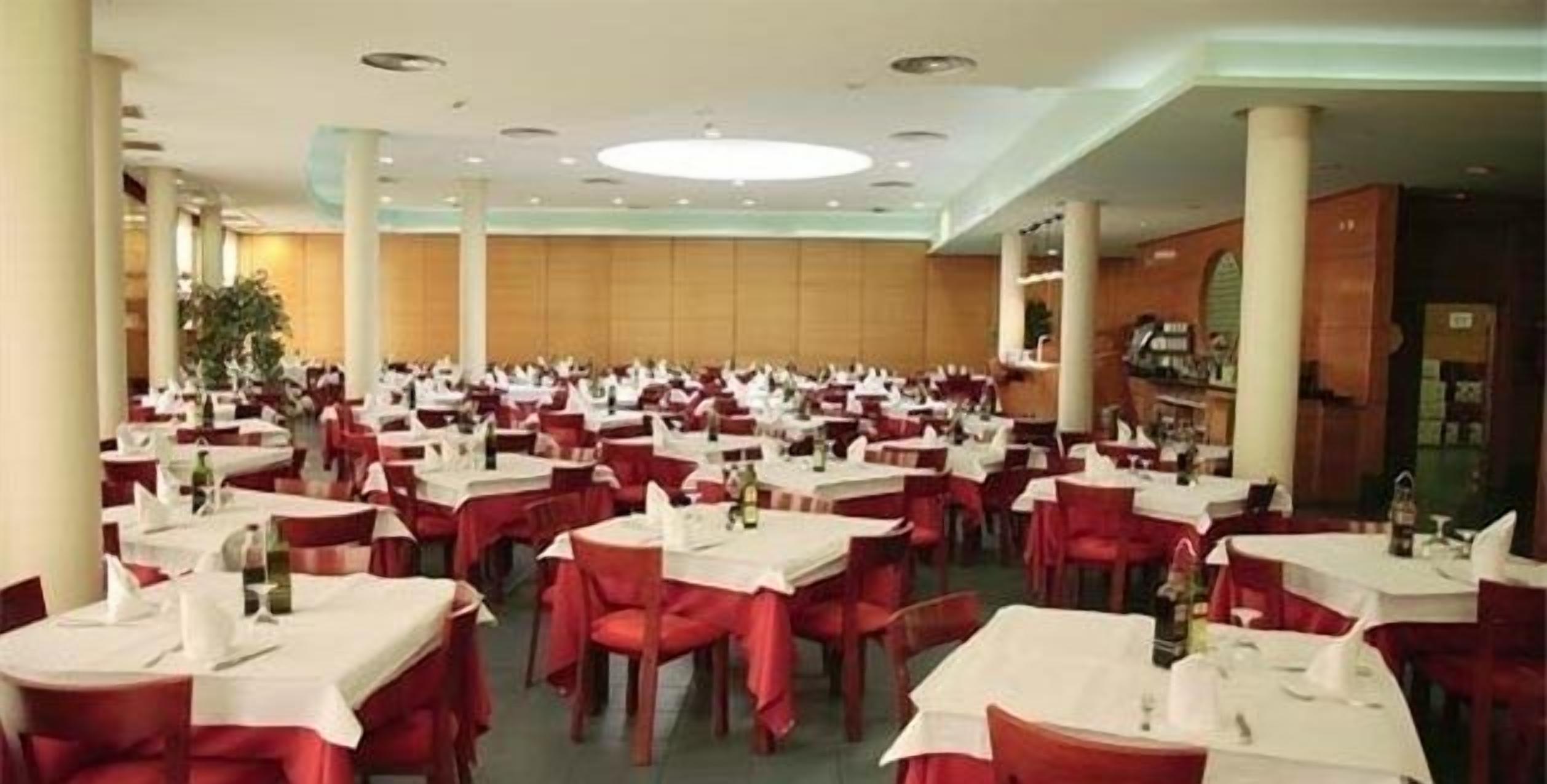 A large banquet hall with round tables covered in white tablecloths and red chairs, arranged in rows.