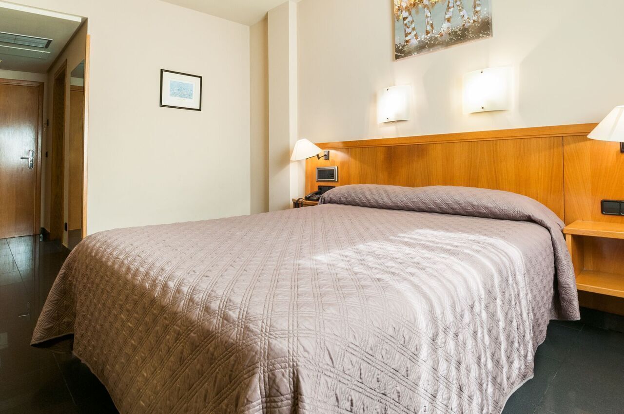 Una habitación de hotel con una cama grande, un cabecero de madera, una mesita de noche con lámpara y un cuadro en la pared.