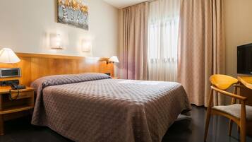 A hotel room with a bed, bedside lamps, a desk with a chair, a television, and a painting on the wall.