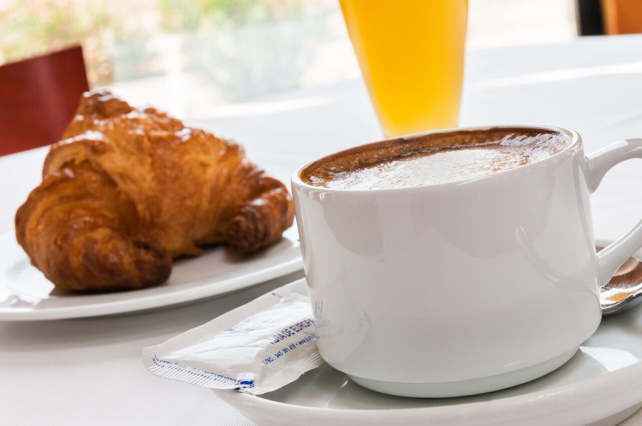 Et croissanter og en kop kaffe på en hvid tallerken.