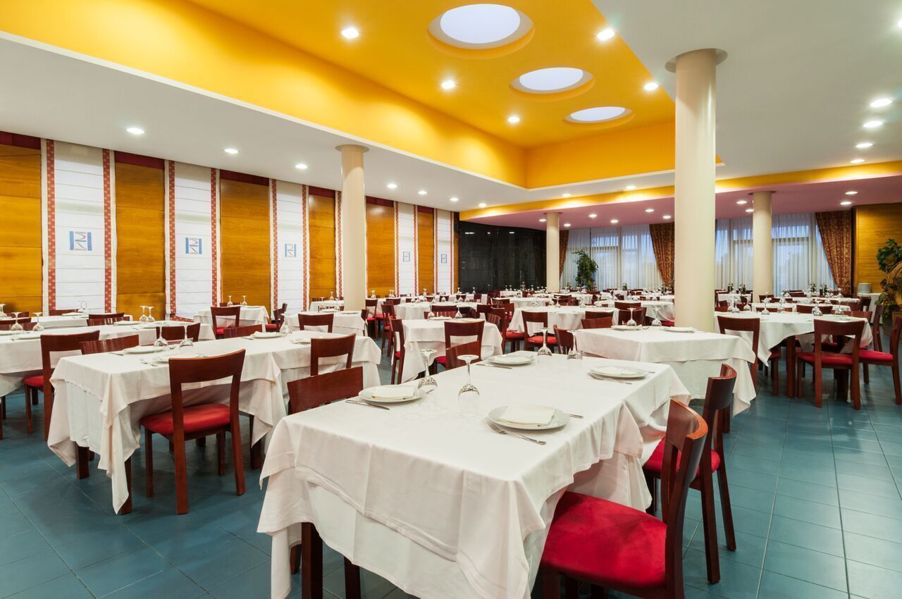 A large dining hall with multiple tables and chairs, arranged in rows.
