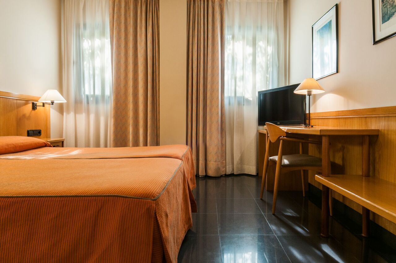 Habitación de hotel con cama, escritorio, silla, televisor y cortinas.