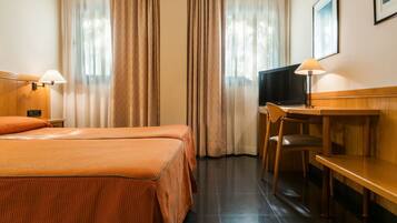 Habitación de hotel con cama, escritorio, silla, televisor y cortinas.