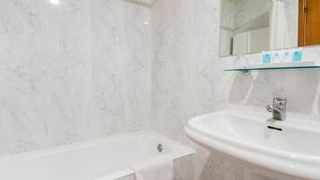 A bathroom with a marble wall, a glass shelf above the sink, and a wooden door.