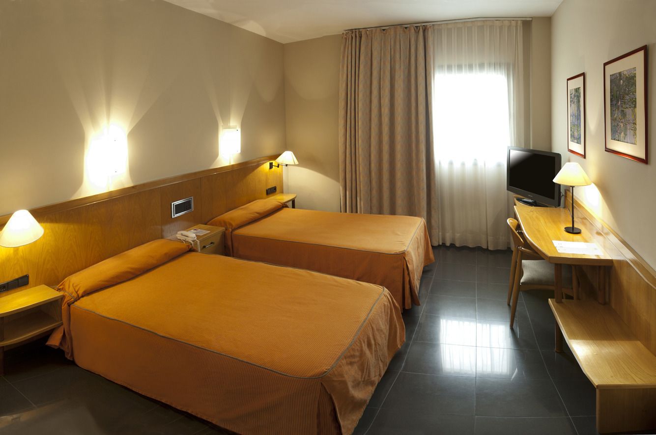 Une chambre d’hôtel avec deux lits, un bureau, une télévision et une fenêtre avec des rideaux.