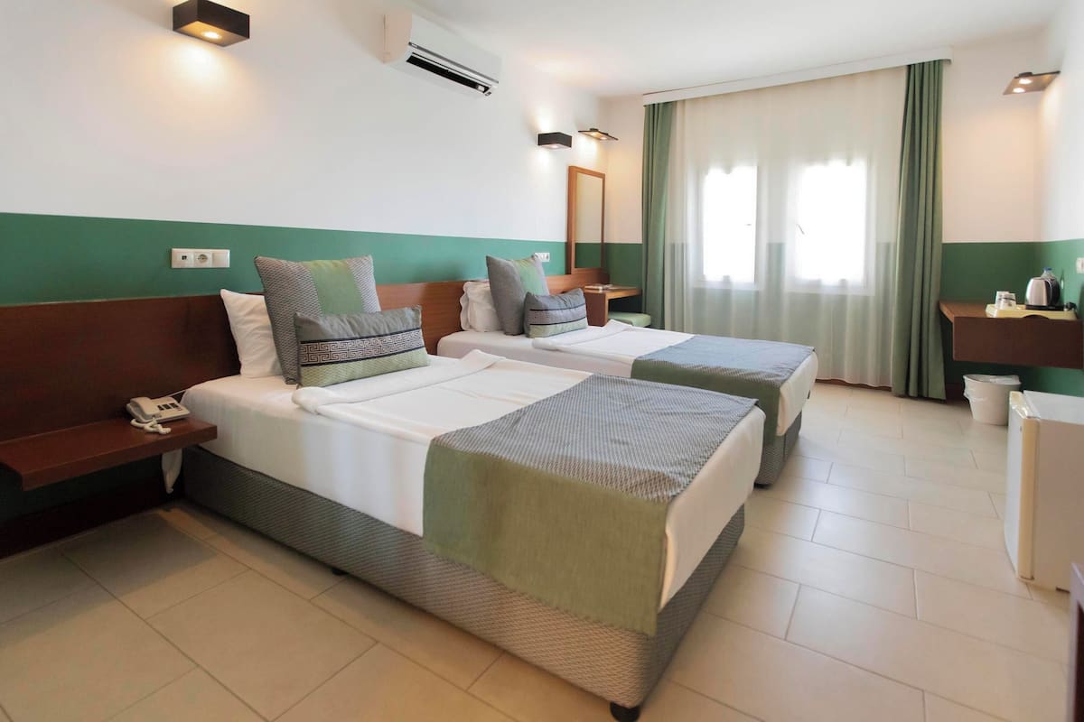 A hotel room with two beds, a desk, a mirror, and a window with curtains.