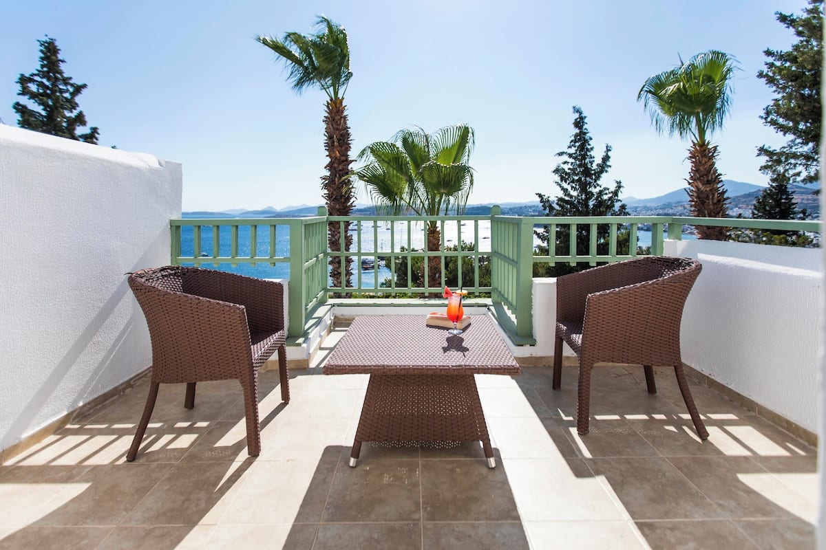 A terrace with wicker furniture, a table, and a view of the sea and mountains.