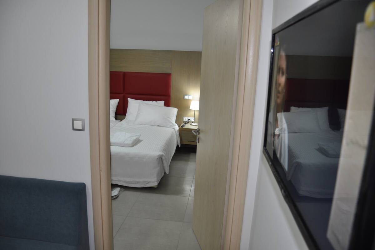 A hotel room with two beds, a red headboard, a nightstand with a lamp, and a large mirror.