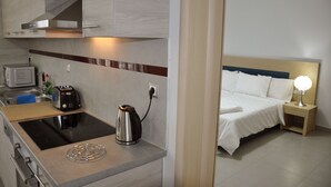 A modern kitchen with a microwave, toaster, kettle, and a stove. Adjacent is a bedroom with a bed, nightstand, and lamp. - Daniel Luxury Apartments (Rhodes)