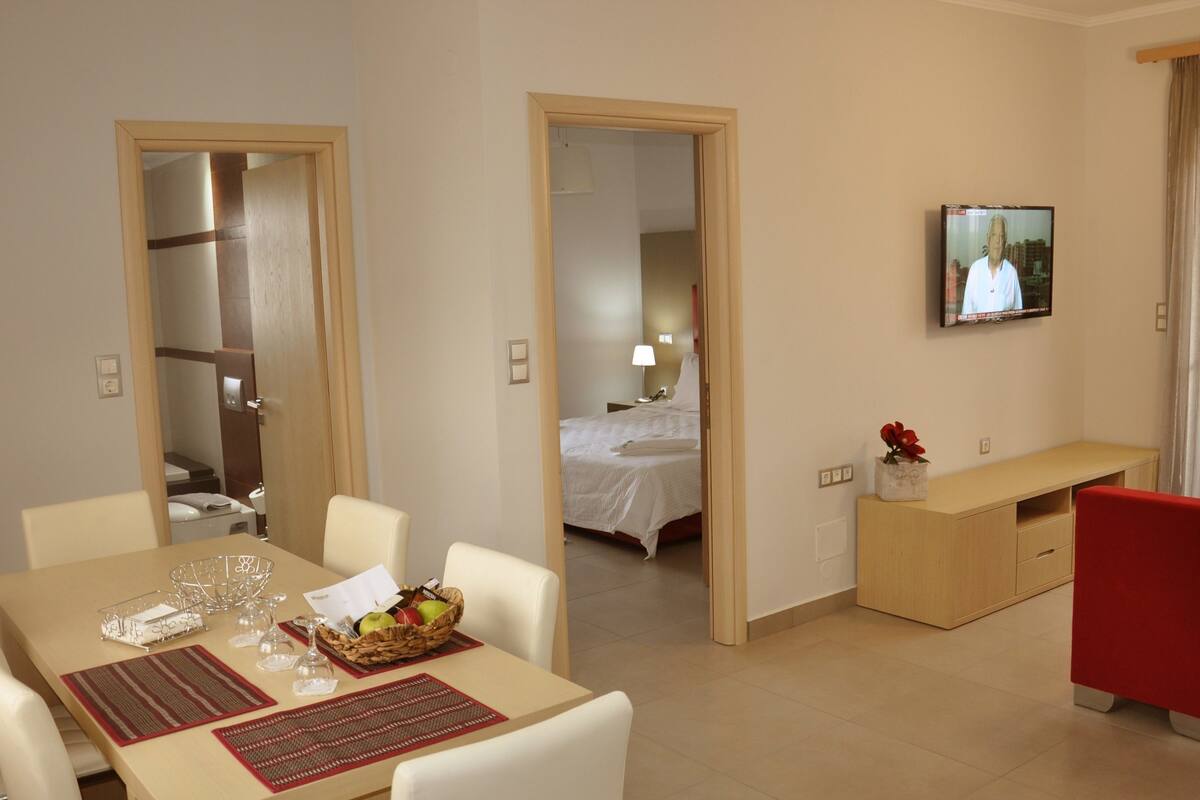 A hotel room with a dining area, a bed, a TV, and a bathroom.