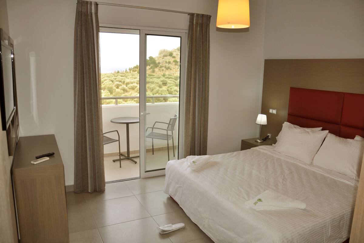 A hotel room with a bed, a desk, a chair, and a balcony with a view.
