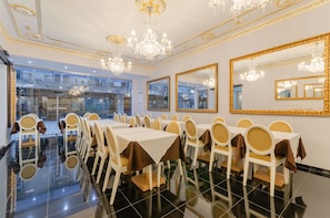 Una sala da pranzo formale con diversi tavoli e sedie, ampi specchi, lampadari e un pavimento lucido.