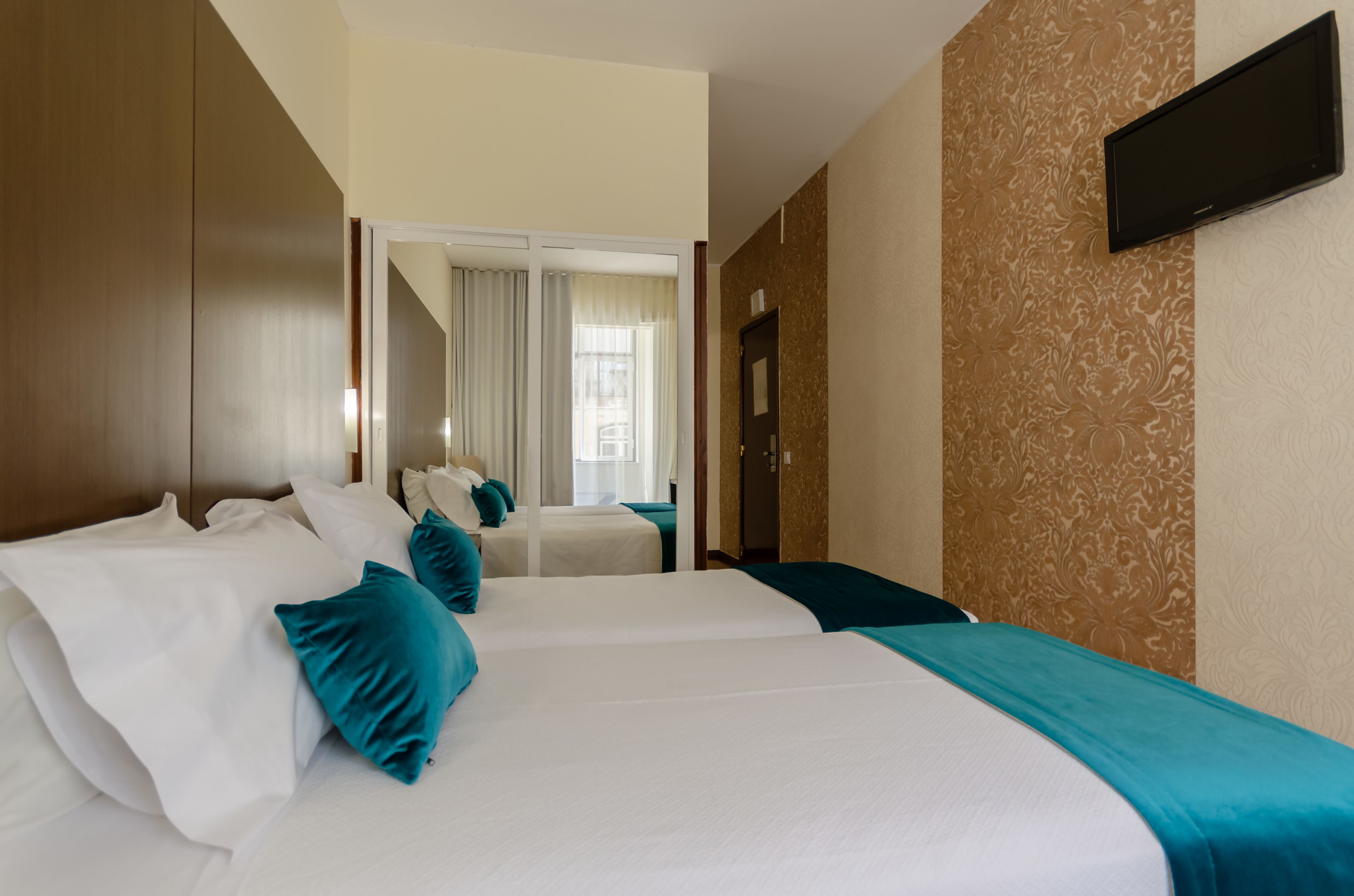 A hotel room with two beds, a TV mounted on the wall, and a mirror reflecting the room.