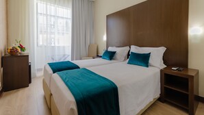 A hotel room with two beds, a wooden headboard, a nightstand with a remote, and a desk with a vase of flowers. - Hotel LX Rossio (Lisbon)