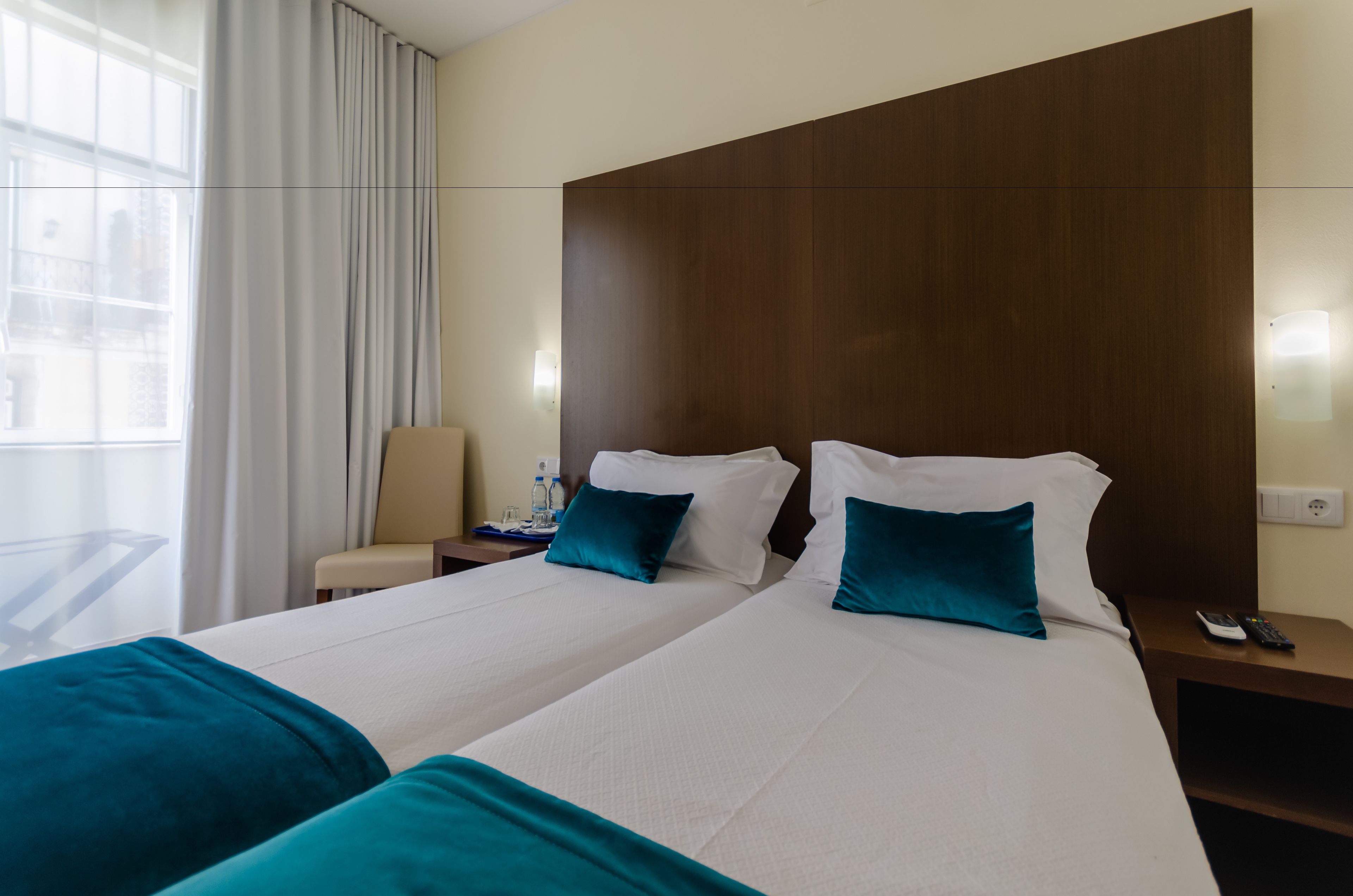 Camera d'albergo con due letti, un comodino, una sedia e una finestra con tende.