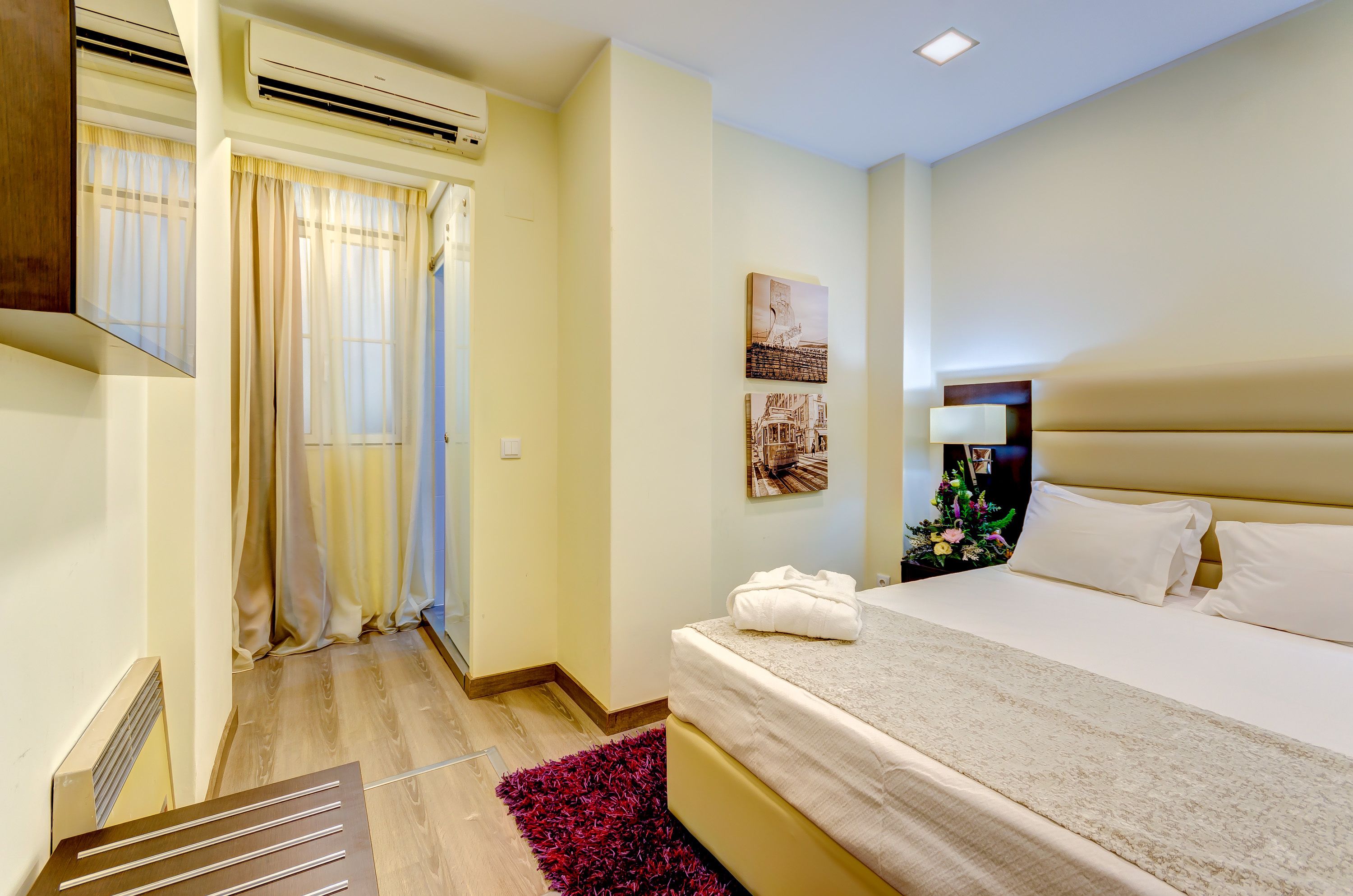 A hotel room with a bed, air conditioning unit, curtains, and a wall-mounted picture.
