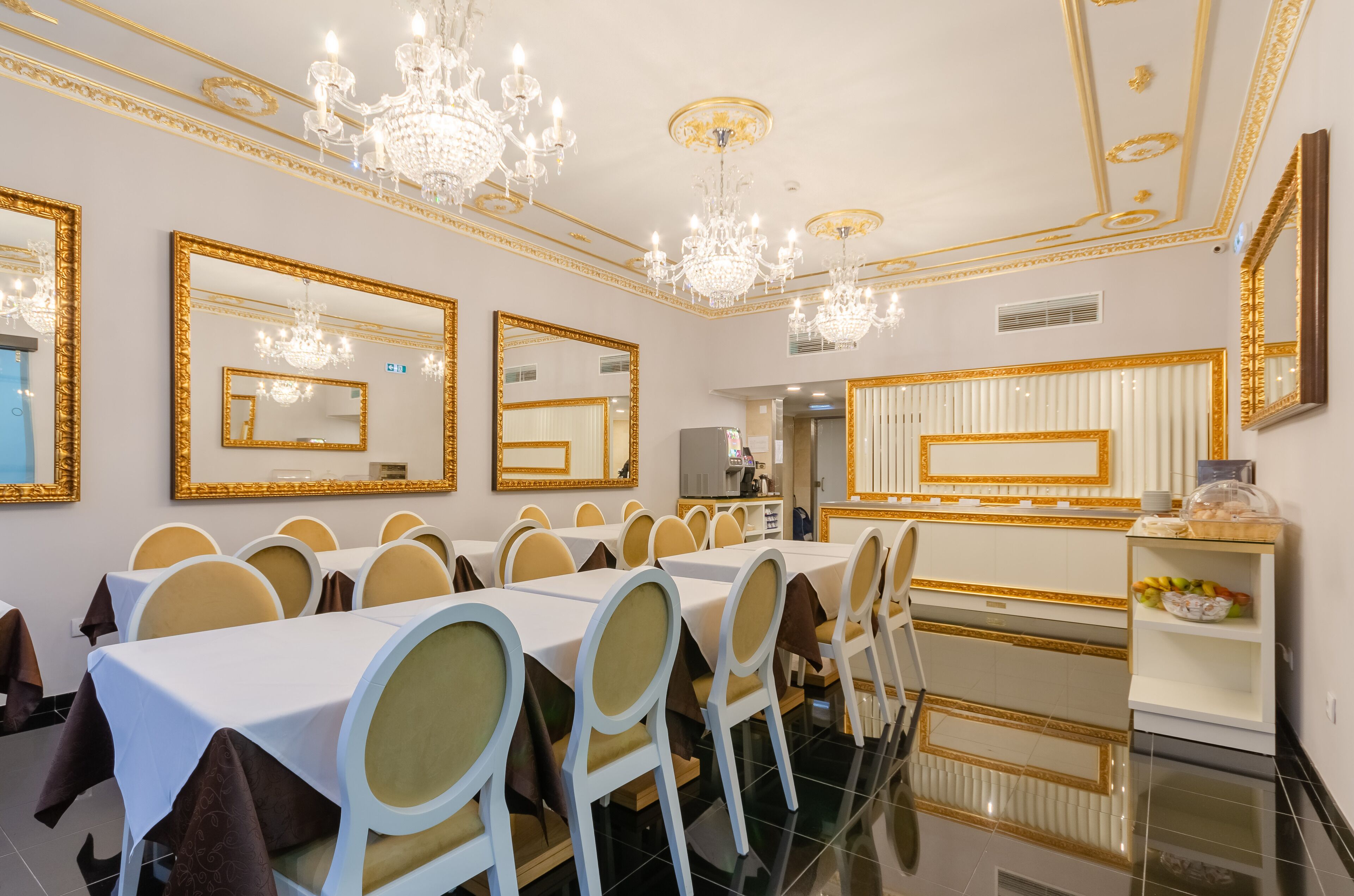 A formal dining room with long tables, gold-framed mirrors, and chandeliers.