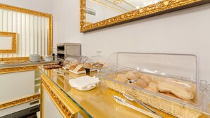 A buffet area with a glass display case containing bread and pastries, a white countertop with a gold frame, and a large mirror with a gold frame. - Hotel LX Rossio (Lisbon)