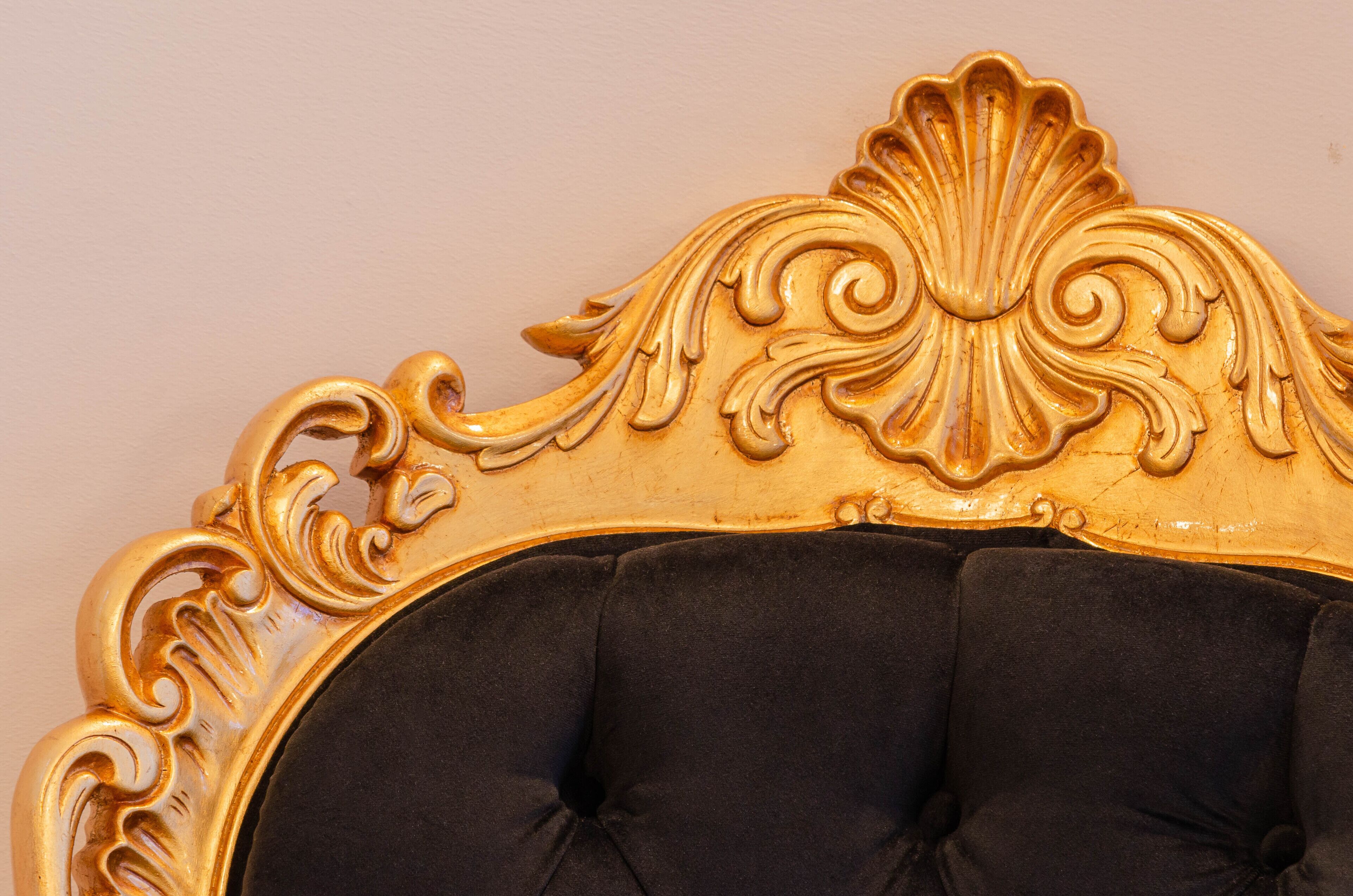 A close-up of a gold ornate headboard with a tufted black upholstered headrest.