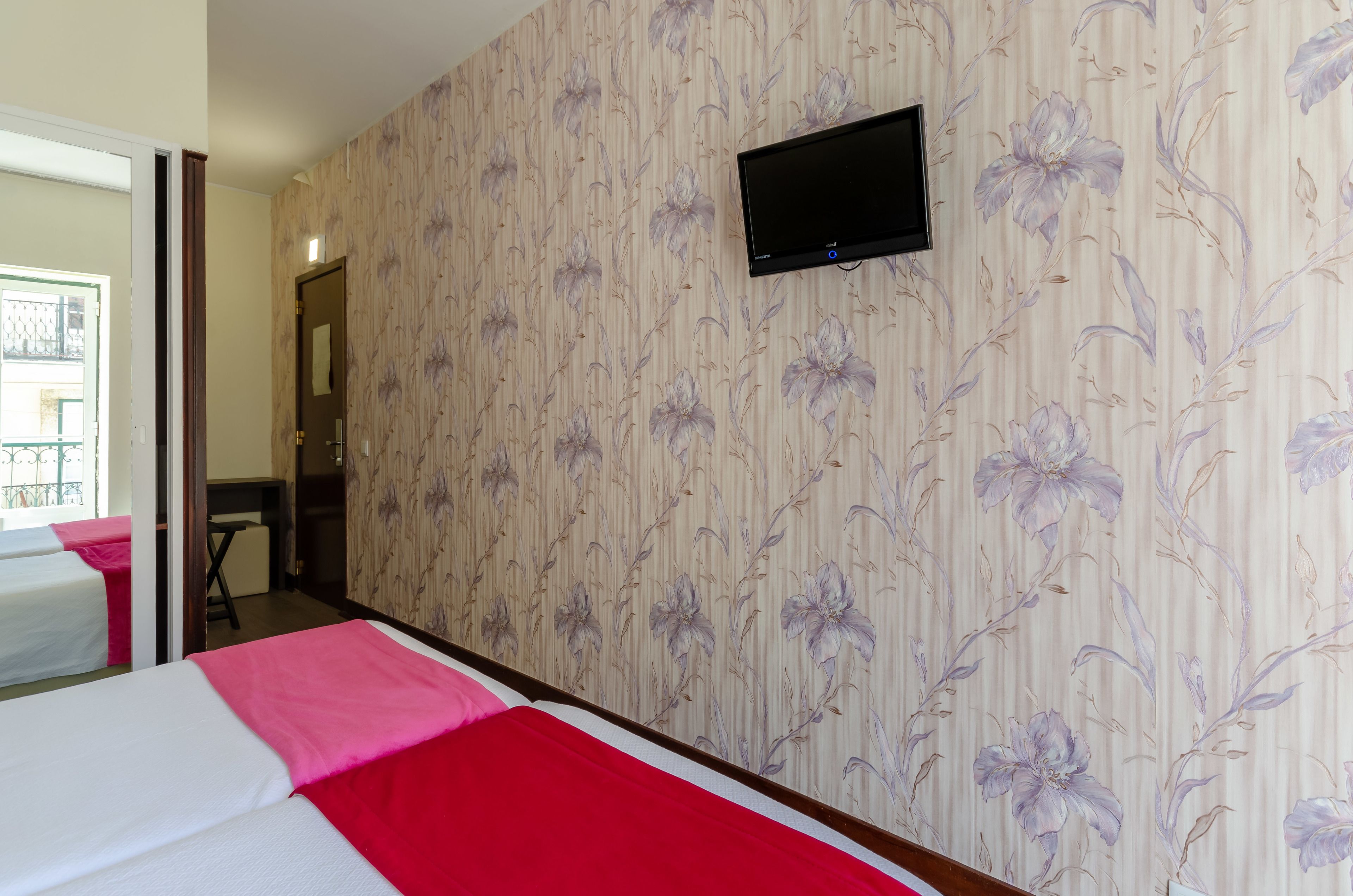 A hotel room with a bed, a TV mounted on the wall, and a door leading to a balcony.