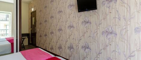 Una habitación de hotel con una cama, un televisor montado en la pared y una puerta que da a un balcón.