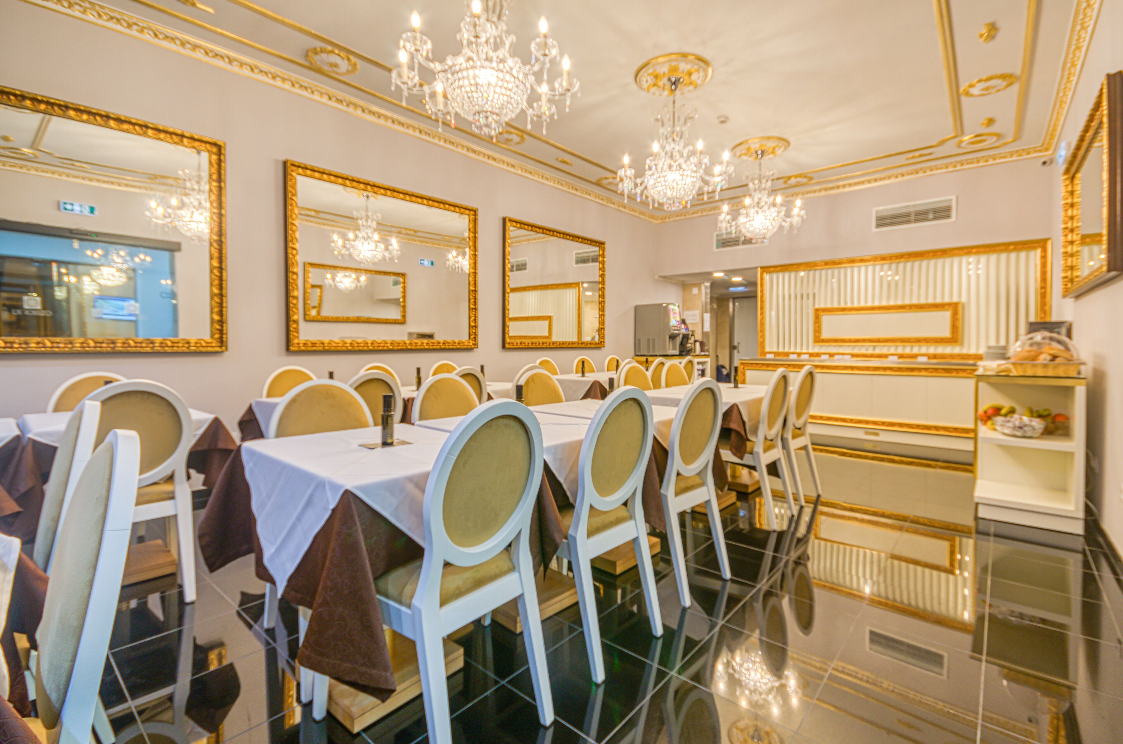 Une salle à manger élégante, avec des tables et des chaises, des lustres et de grands miroirs aux murs.