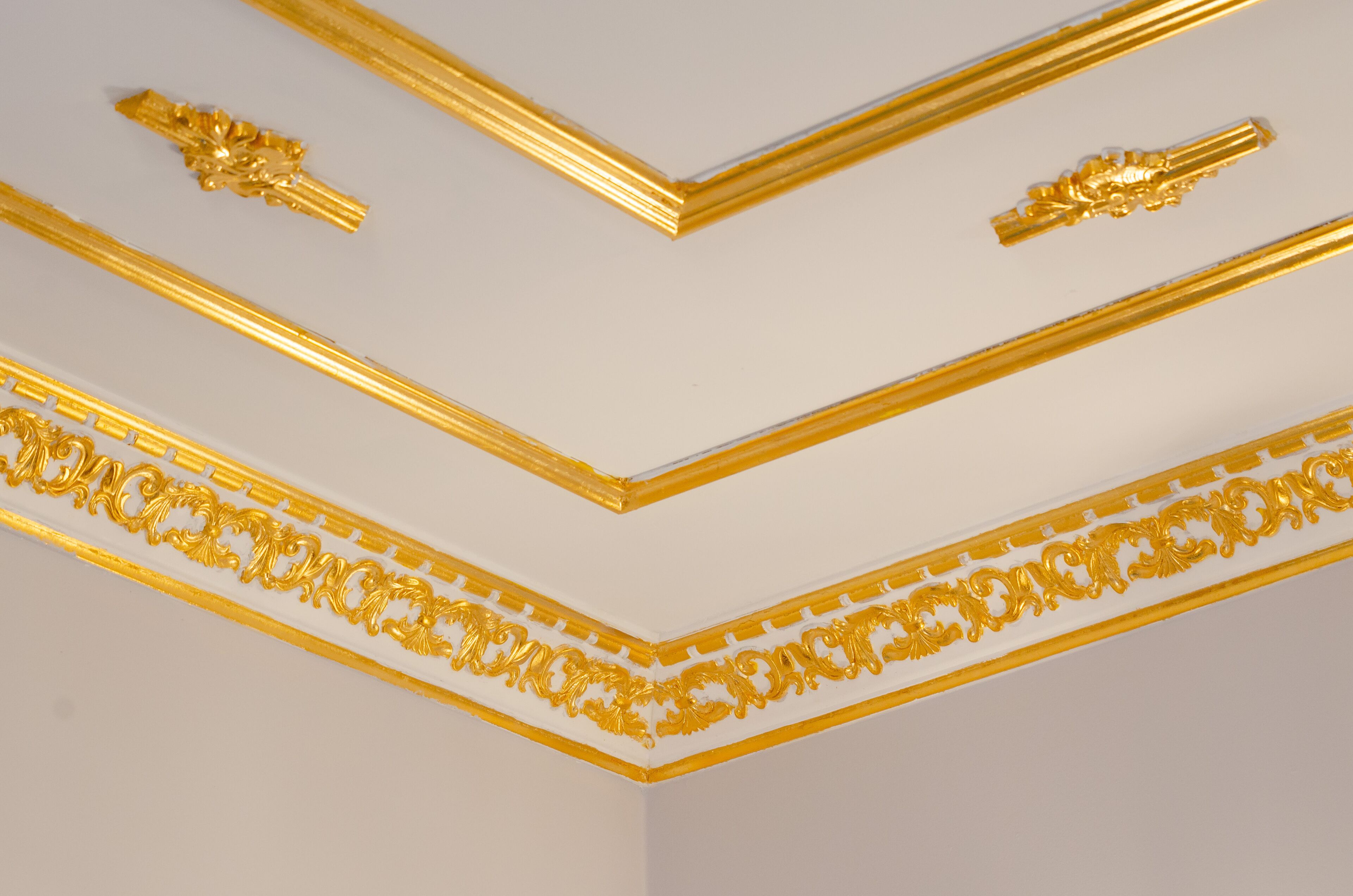 Un plafond orné de moulures décoratives dorées sur un fond blanc.