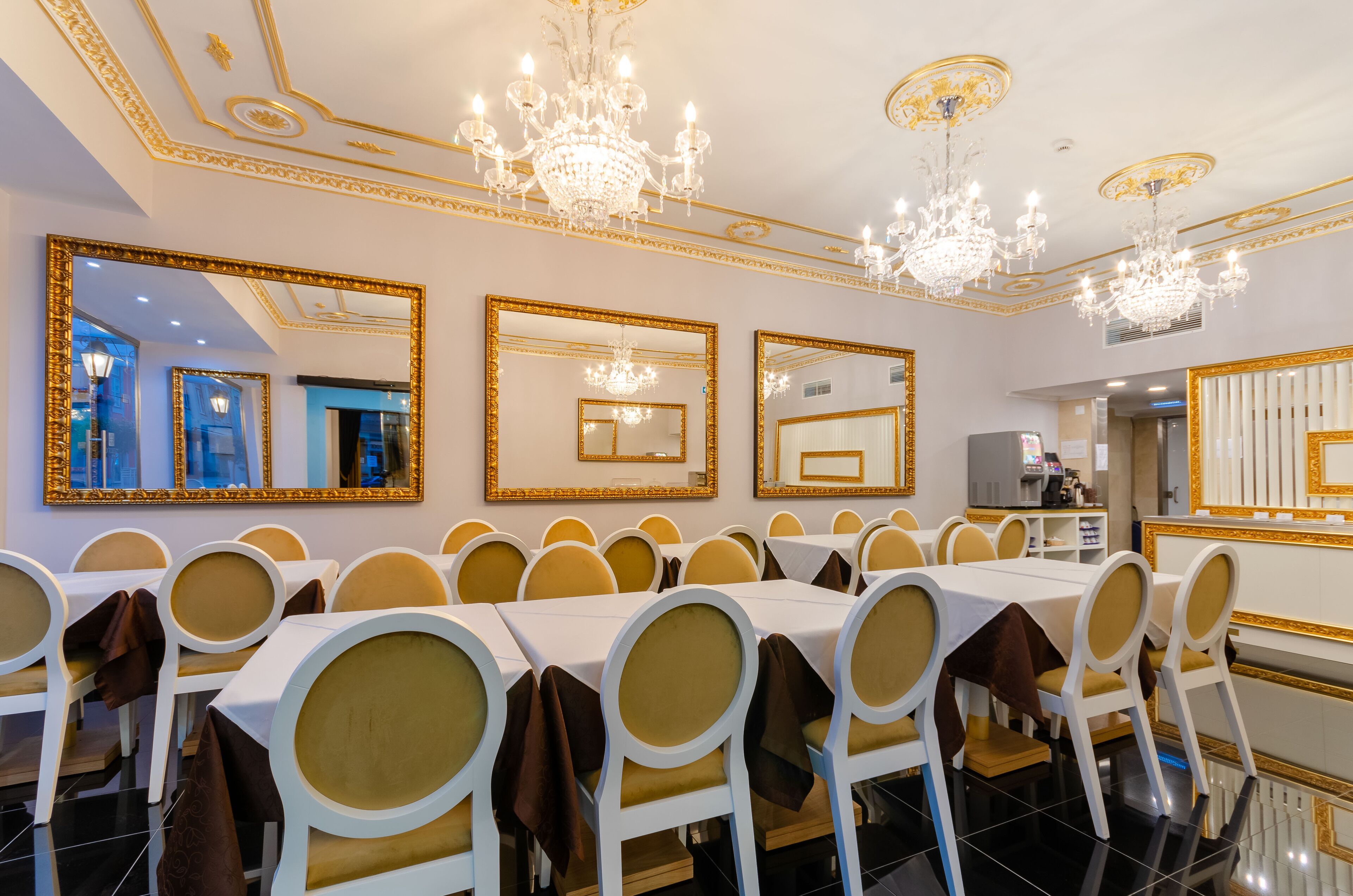 A banquet hall with long tables, golden chairs, and ornate chandeliers.